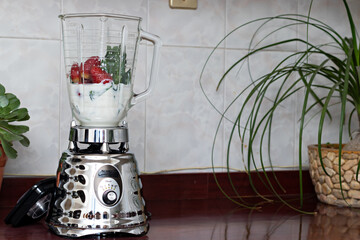 blender with milk, spinach and strawberries on a kitchen counter