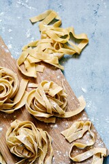 Raw yellow homemade italian pasta pappardelle, fettuccine or tagliatelle on a blue background, close up. Egg homemade noodles cooking process, long rolled macaroni, uncooked spaghetti .