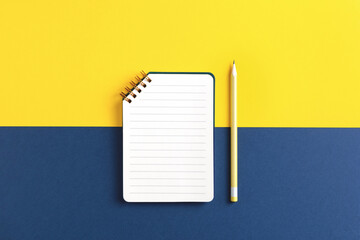 Open spiral ruled notebook with pencil on yellow and blue background. Top view.