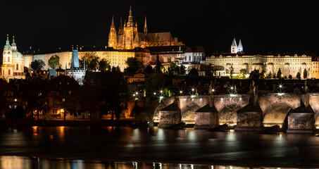 prague castle and charles bridge and st. vita church lights from street lights are reflected on the surface of the vltava river in the center of prague at night in the czech republic