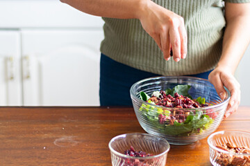 Hands of a woman adding cranberries to a bowl of salad
