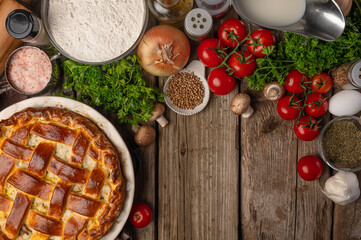 Appetizing pie with meat and mushrooms on wooden table with variety of ingredients background. Cooking process. Backstage of preparing tasty meal. View from above. Flat lay. Cookbook. Space for text.