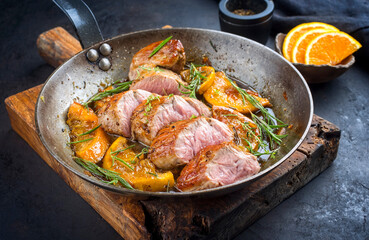 Traditional fried pork filet medaillons in with caramelized orange slices and herbs served as close-up in a rustic wrought iron skillet