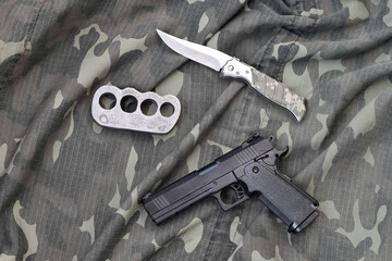Handgun lies with brass knuckles and knife on camouflage military uniform close up. Concept of...