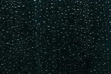 Raindrops on dark blue-green window glass as background