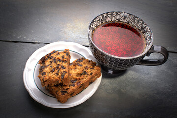 The hot cup of tea and two slices of fruit cake on stone table