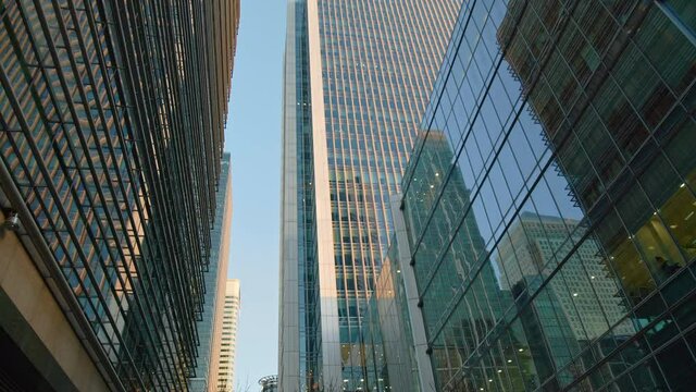 A cinematic look to tall business Skyscrapers in Canary Wharf, London, UK in 4K. Unrecognisable financial and banks buildings with glass walls in a sunny day with clear sky.