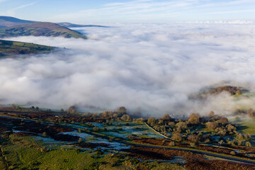Aerial view of a narrow, winding mountain road on a hillside above a fog filled valley