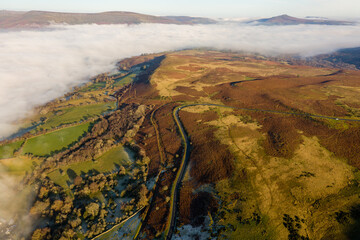 Aerial view of a narrow, winding mountain road emerging through a bank of fog and low cloud on a cold, frosty day