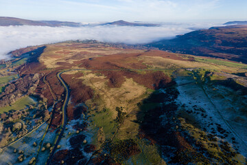 Aerial view of a narrow, winding mountain road on a hillside above a fog filled valley