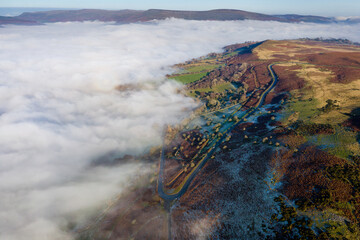 Aerial view of a narrow, winding mountain road on a hillside above a fog filled valley