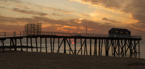 Orange sunrise behind a long, wooden fishing pier on the Atlantic Ocean.