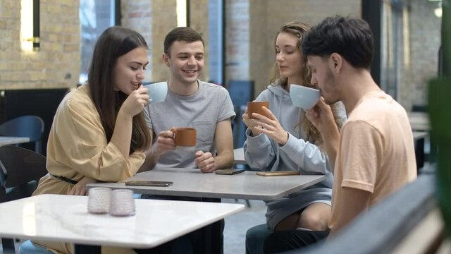 Positive young woman toasting and clinking coffee cups with friends in cafe. Beautiful Caucasian lady sharing good news with group of people. Friendship and leisure. Cinema 4k ProRes HQ.