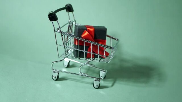 Gift box with red ribbon falling into shopping cart. Buy presents online. E-commerce purchase 