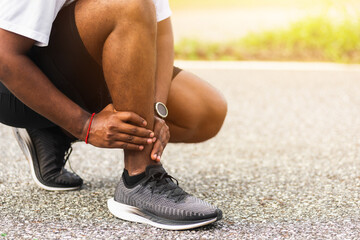 Close up Asian young sport runner black man wear watch hands joint hold leg pain because of twisted ankle broken while running at the outdoor street health park, healthy exercise Injury from workout - Powered by Adobe