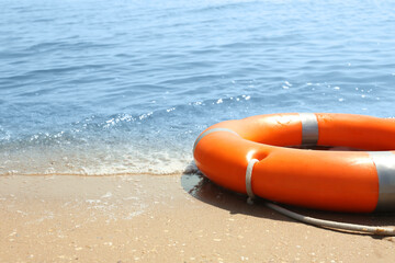 Orange life buoy on sand near sea, closeup. Emergency rescue equipment