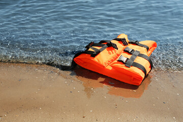 Orange life jacket on sand near sea. Emergency rescue equipment