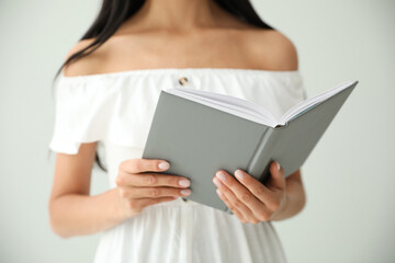 Young woman reading book on light grey background, closeup