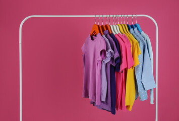 Rack with stylish children clothes on pink background