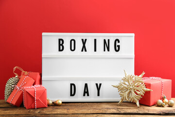 Composition with Boxing Day sign and Christmas gifts on wooden table against red background