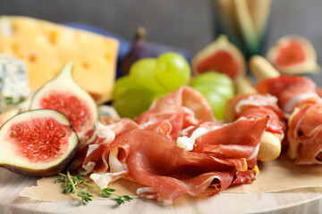 Board with delicious figs, cheese, grapes and bread with proscuitto, closeup