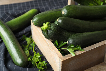 Crate with green zucchinis and parsley on table, closeup