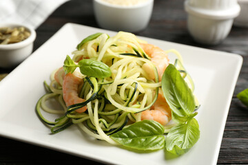 Delicious zucchini pasta with shrimps and basil on black wooden table, closeup