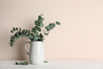 Vase with beautiful eucalyptus branches on white wooden table near beige wall. Space for text © New Africa