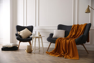 Comfortable sofa with knitted blanket, armchair and coffee table in stylish room interior