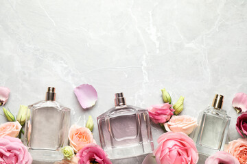 Flat lay composition of different perfume bottles and flowers on light grey marble background,...