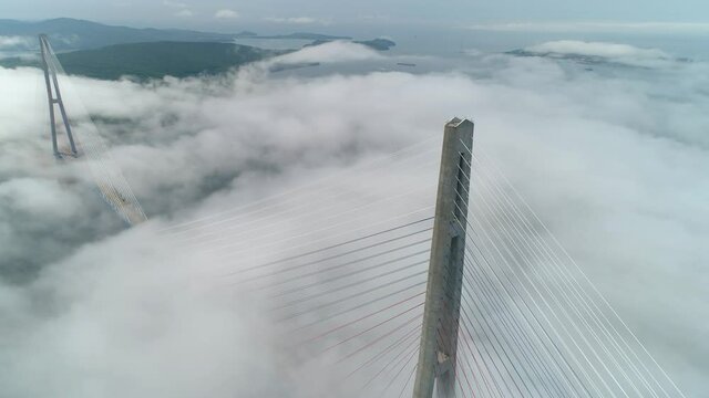 Aerial epic Russian Bridge Vladivostok symbol of city modern landmark, unique weather condition fog-cowered foggy low cumulus clouds. Pillons of cables above. Inspirational emotional footage Russia
