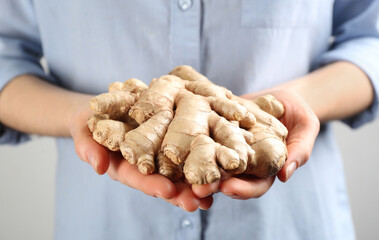 Woman holding pile of ginger roots on light background, closeup. Natural antibiotic