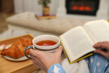 Woman with cup of tea and book resting at home, closeup