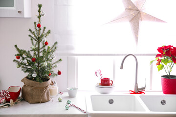 Small Christmas tree decorated with baubles and festive lights in kitchen