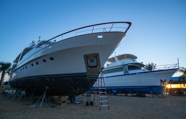 Two large vessels rest on boat stands in a Florida boatyard