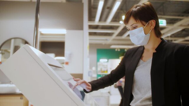 Woman customer wearing medical mask searching for information in interactive wayfinding kiosk in shopping mall. Easy and safety shopping during pandemic. Shopping mall indoor navigation.
