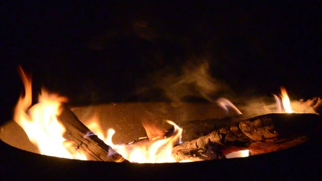 close up of flaming logs and smoke in an outdoor fire pit