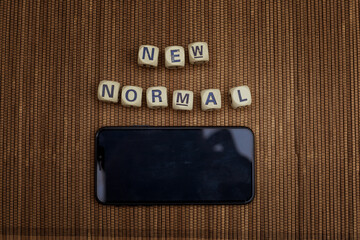Smart phone with words new normal on wooden blocks.