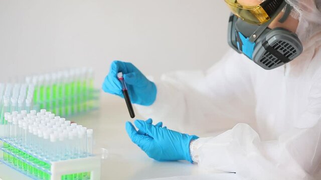Doctor in a white protective overalls and a respirator take a test tube with blood sample from holder. FHD video.