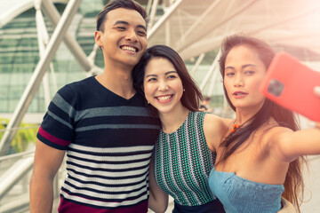Three asian young friends outdoor taking selfies. City life of two girls and one boy