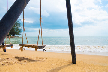 Selective focus at wooden swing on sand at the beach. With wave and sea view with cloud, blue sky. Summer vacation at beautiful tropical island. Travel resort destination.