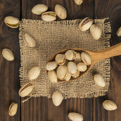 Top view of a wooden spoon with fried pistachios scattered on a piece of burlap.