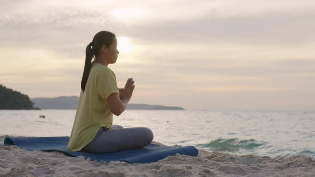 Side view of Asian women Practicing yoga pray on beach sand in morning