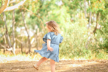 Little girl in pretty blue denim dress twirling in natural outdoor setting