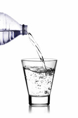 water is poured into a glass glass from a plastic bottle on a white background with a reflection