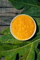 Top View of Papaya or Pawpaw Pulp in a Plate on Green Leaf Isolated on Wooden Background in Vertical Orientation