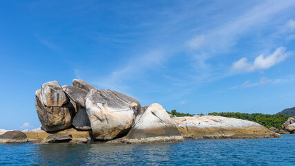 Big stone stack sitting on a small islet next with clear sea water and blue sky background on sunny day