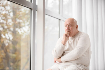 Sad senior man near window in clinic. Prostate cancer awareness concept