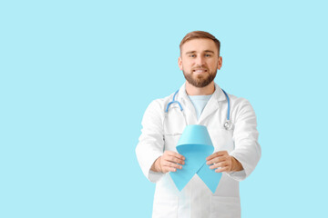 Doctor with blue ribbon on color background. Prostate cancer awareness concept