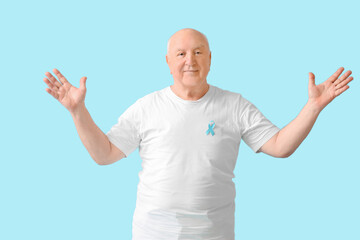 Senior man with blue ribbon on color background. Prostate cancer awareness concept